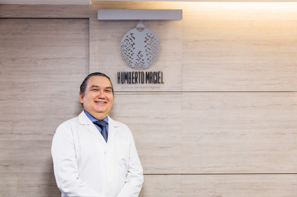 Médico dermatologista, Dr. Humberto Maciel olhando para a câmera e sorrindo. Na recepção de sua clinica.