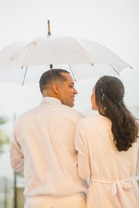 close do noivo olhando apaixonado para a noiva segurando guarda chuva branco sob muita chuva.