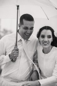 close de noivos sorridentes fugindo da chuva, Noiva começando a correr e o noivo segurando o guarda chuva
